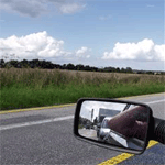 A side view mirror of a motorcycle on a road.
