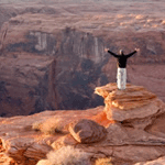 A man standing on top of a cliff with his arms outstretched.