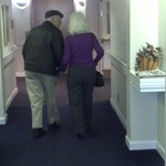 An elderly couple walking down a hallway.